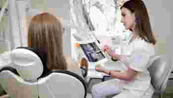 Врач имплантолог(женщина) показывает пациенту(женщина), сидящему в кресле рентгеновский снимок