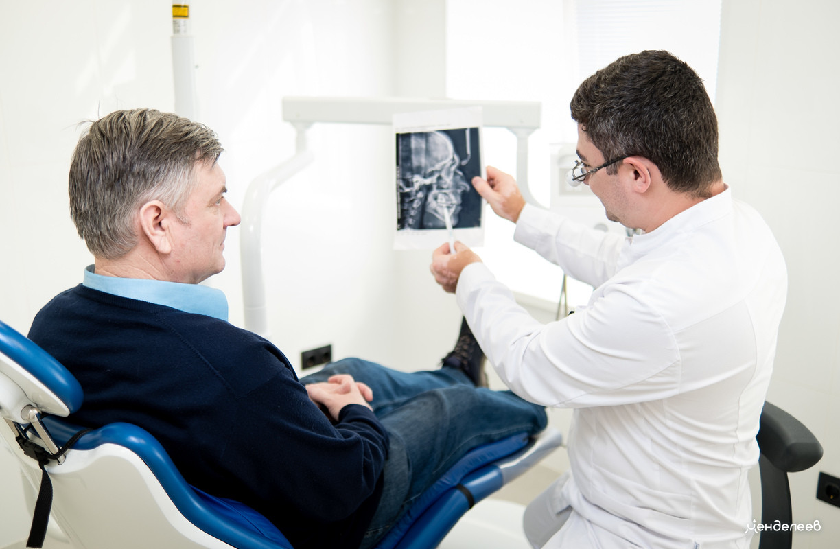 стоматолог показывает на снимке проблему пациенту